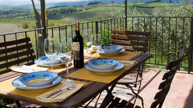 A table set for two with wine glasses, plates, and a bottle on a balcony overlooking a vineyard. - La Canonica (Montalcino)