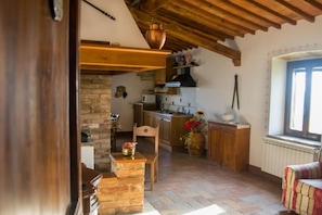 A rustic kitchen with exposed wooden beams, a brick wall, and a stone fireplace. - La Canonica (Montalcino)