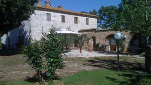 A stone building with a garden area, including a small tree and a white umbrella. - La Canonica (Montalcino)