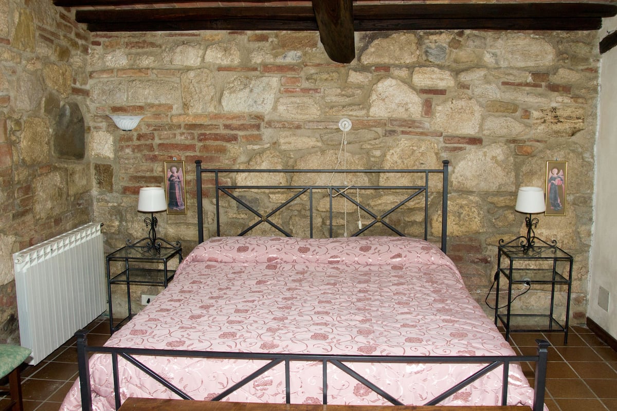 A room with a stone wall, a bed with a patterned bedspread, two bedside tables with lamps, and a radiator.