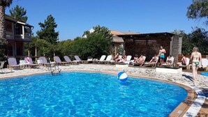 A swimming pool with lounge chairs and a beach ball, surrounded by trees and a building.