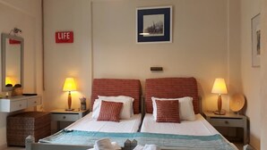 A hotel room with two beds, each with red-striped pillows, a framed picture on the wall, and a 'LIFE' sign.