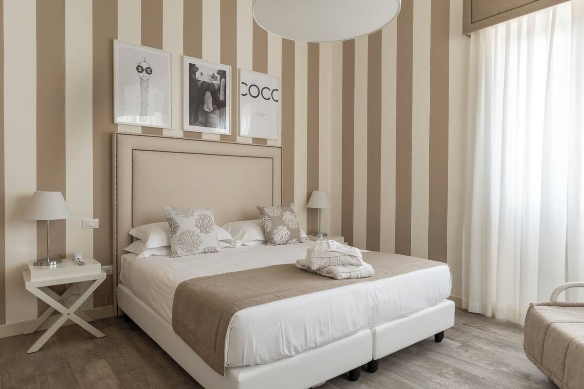 Habitación de hotel con una cama grande, dos mesitas de noche, cabecero y una ventana con cortinas.