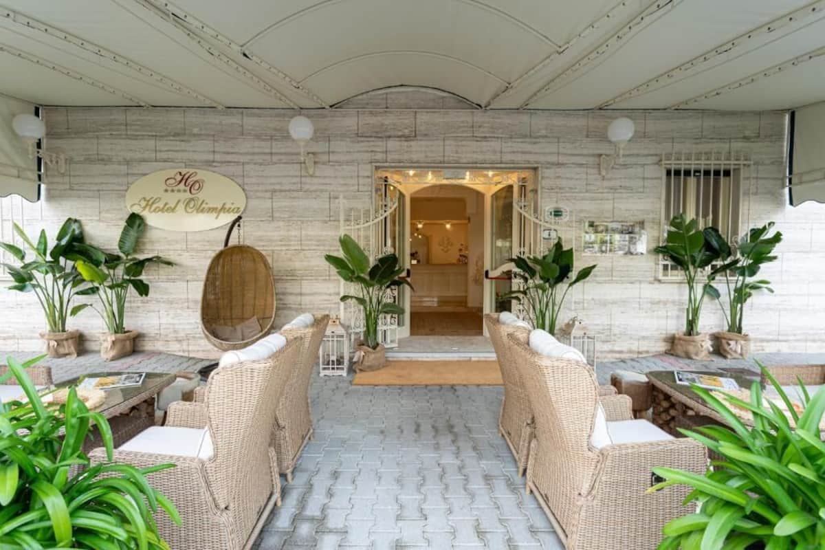 Un vestíbulo de hotel con mobiliario de mimbre, plantas en macetas y un cartel que dice 'Hotel Olimpia'.