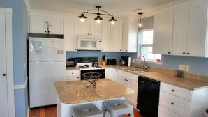 A kitchen with white cabinets, a granite countertop, a refrigerator, a microwave, a stove, a sink, and a dishwasher.