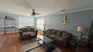 A living room with two sofas, a coffee table, a striped rug, and a ceiling fan.