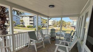 A covered outdoor area with a tiled floor, white railings, and several Adirondack chairs. - The Ocean House 6 Bedroom Home by RedAwning (Surfside Beach)