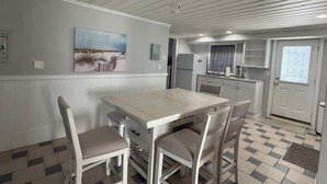 A dining area with a table and chairs, a kitchen with cabinets and appliances, and a door with a window. - The Ocean House 6 Bedroom Home by RedAwning (Surfside Beach)