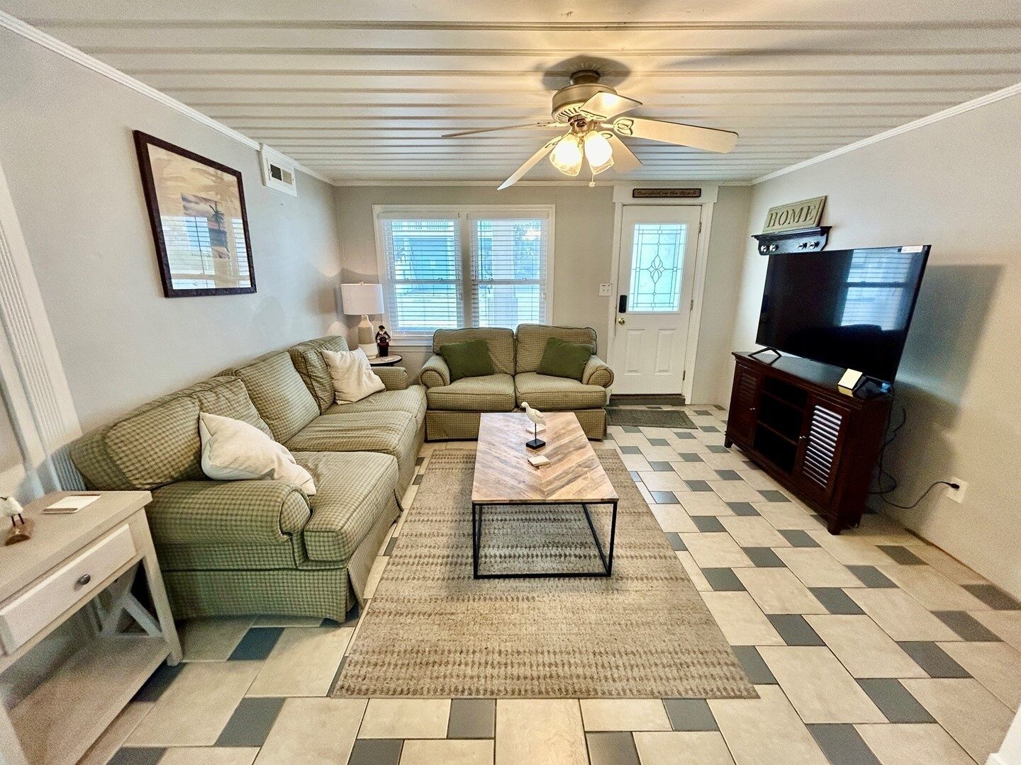 A living room with a sectional sofa, a coffee table, a TV stand, and a ceiling fan.