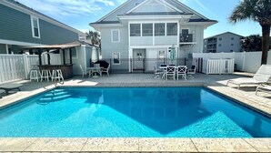 A swimming pool with a patio area, a two-story building, and a white fence. - The Ocean House 6 Bedroom Home by RedAwning (Surfside Beach)