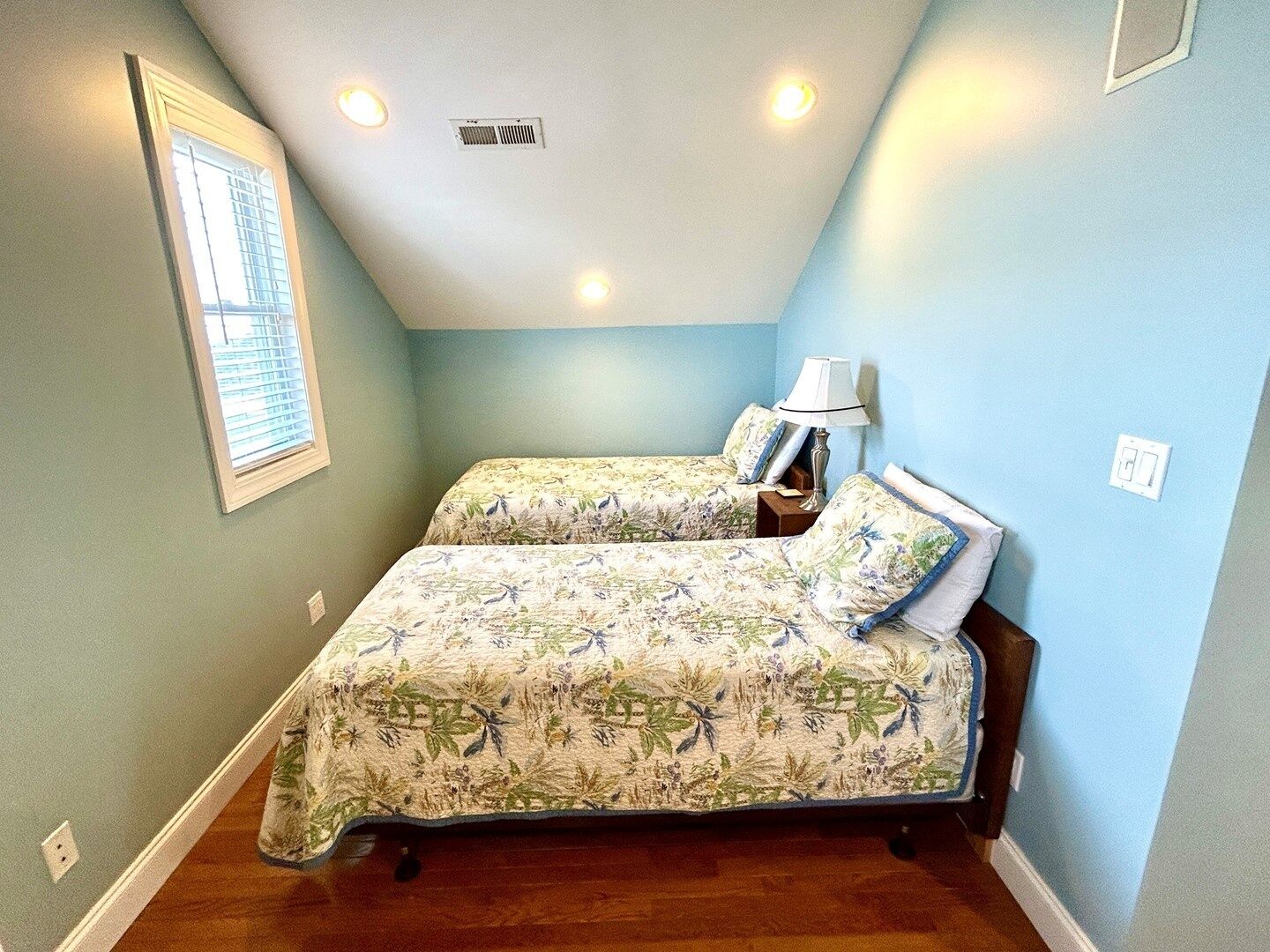 A bedroom with two beds, a window, and a ceiling vent.