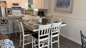 A dining area with a wooden table, white chairs, and a painting on the wall. - 5 By The Sea 5 Bedroom Home by RedAwning (Surfside Beach)