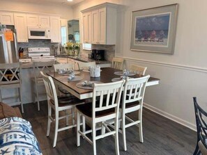 A dining area with a wooden table, white chairs, and a painting on the wall.