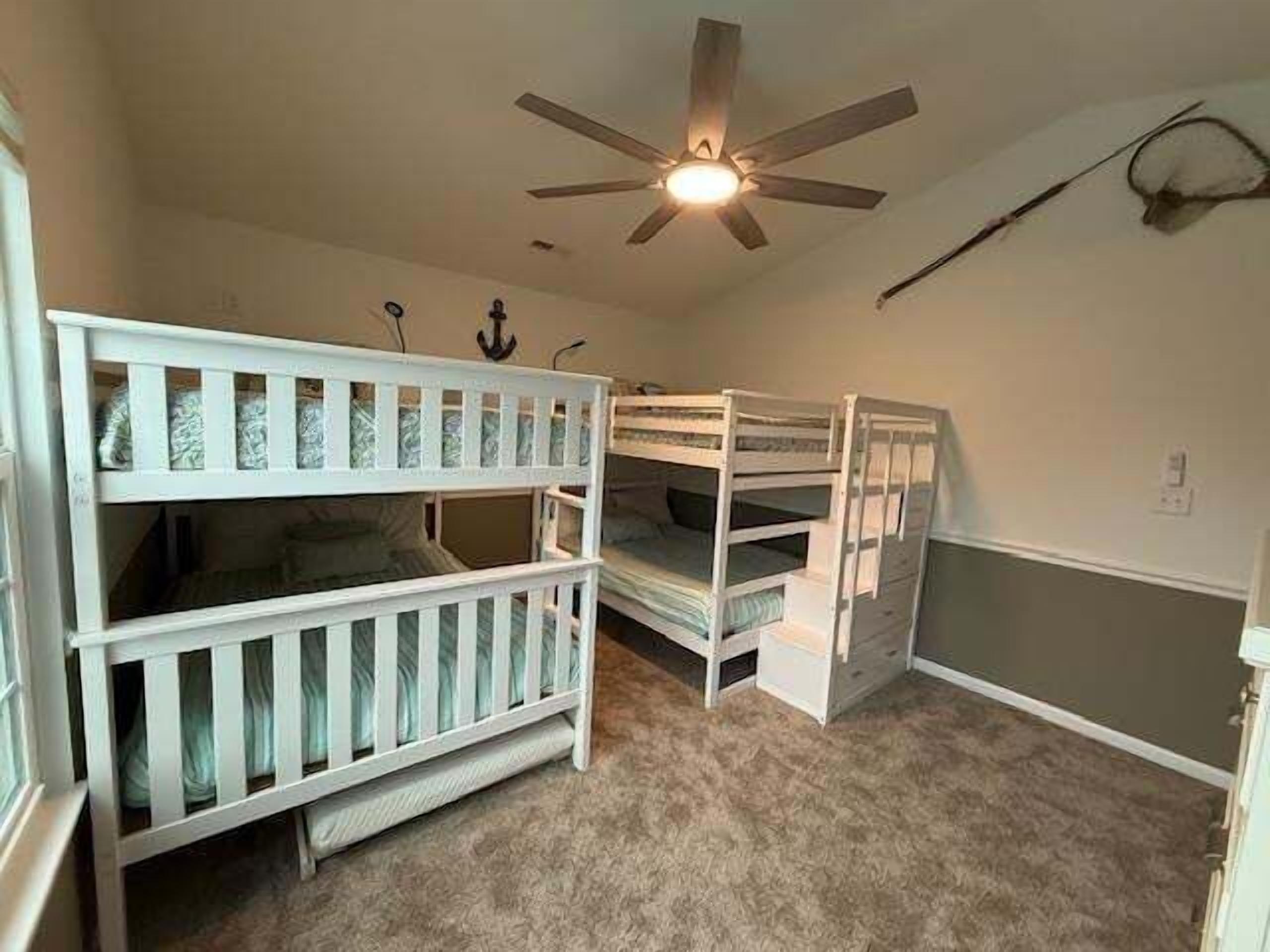 A room with bunk beds, a ceiling fan, and a carpeted floor.