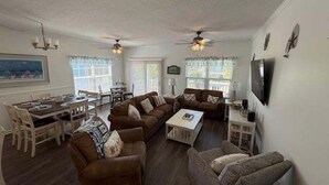 A spacious living room with a dining area, two ceiling fans, and a flat-screen TV mounted on the wall. - 5 By The Sea 5 Bedroom Home by RedAwning (Surfside Beach)