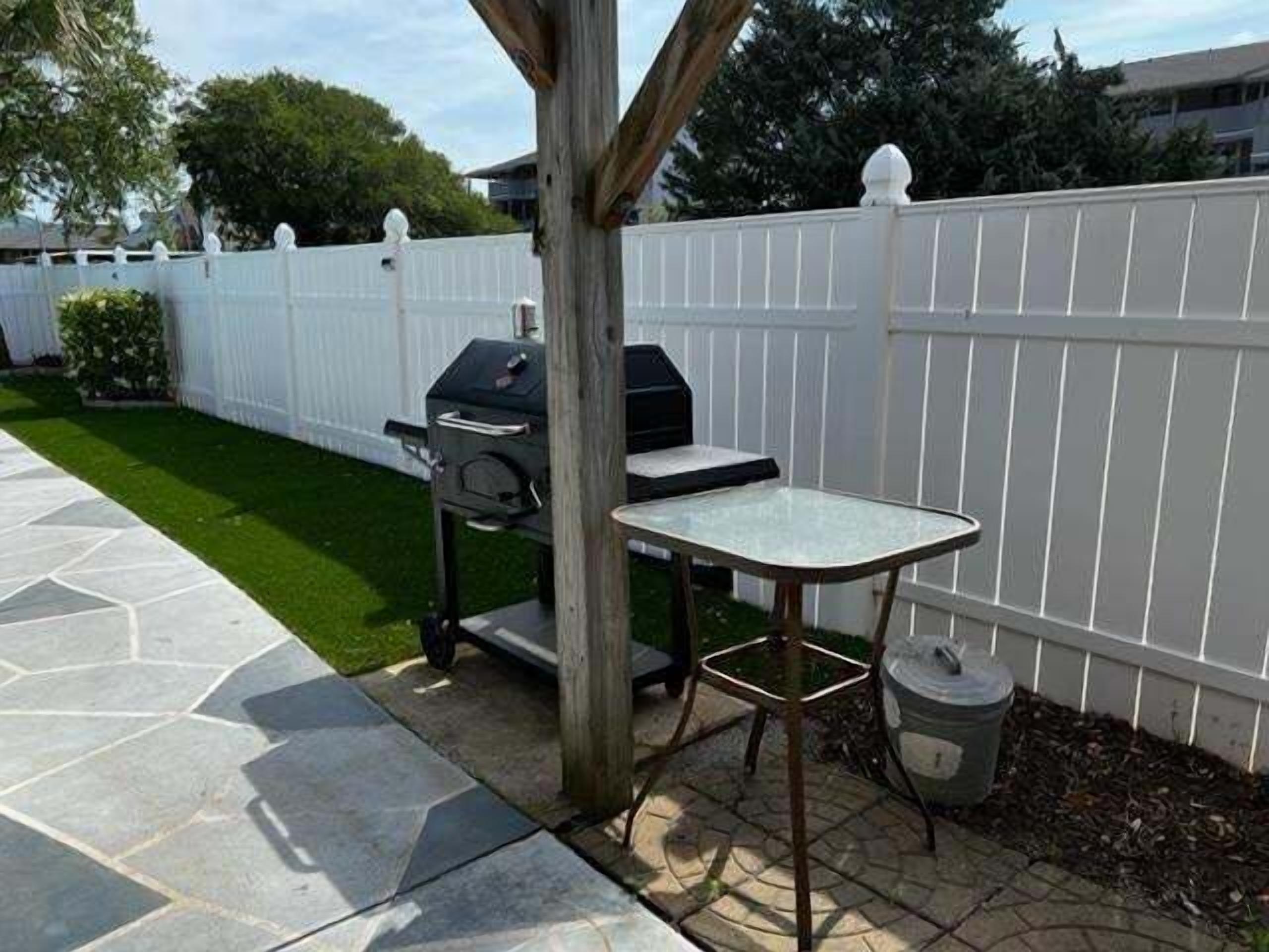 A patio with a grill, a table, and a trash can.