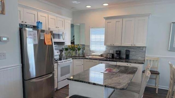 A modern kitchen with white cabinetry, a stainless steel refrigerator, a built-in oven, and a granite countertop. - 5 By The Sea 5 Bedroom Home by RedAwning (Surfside Beach)
