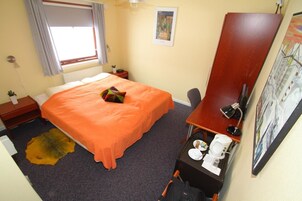 Habitación de hotel con cama, escritorio con silla, lámpara de escritorio, cafetera y un cuadro en la pared.