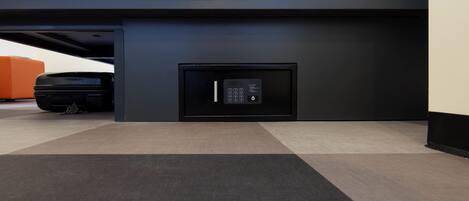 A modern hotel room with a bed, a built-in safe, and a suitcase on the floor.