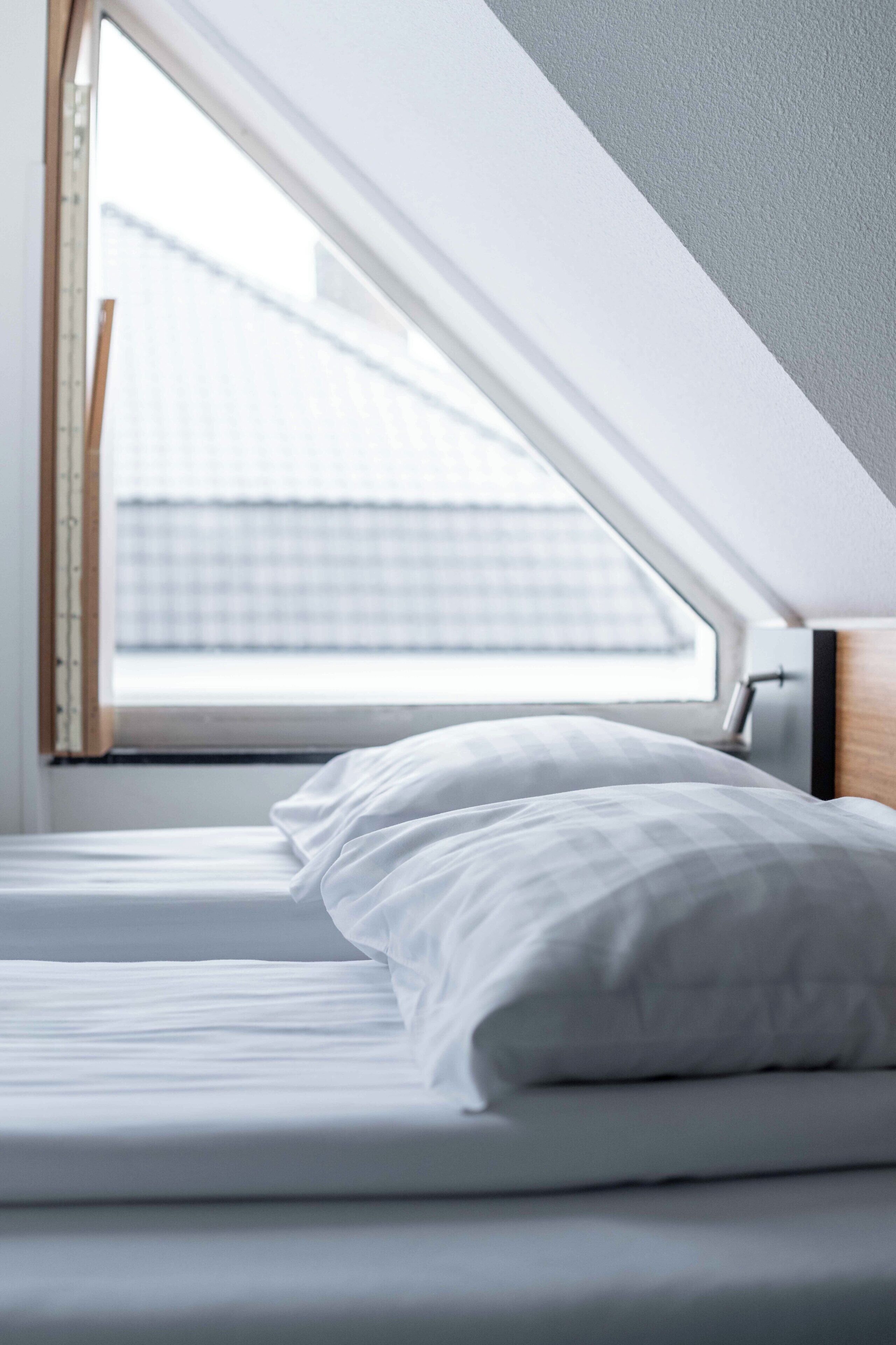A bed in a room with a skylight, a window, and a view of a building outside.
