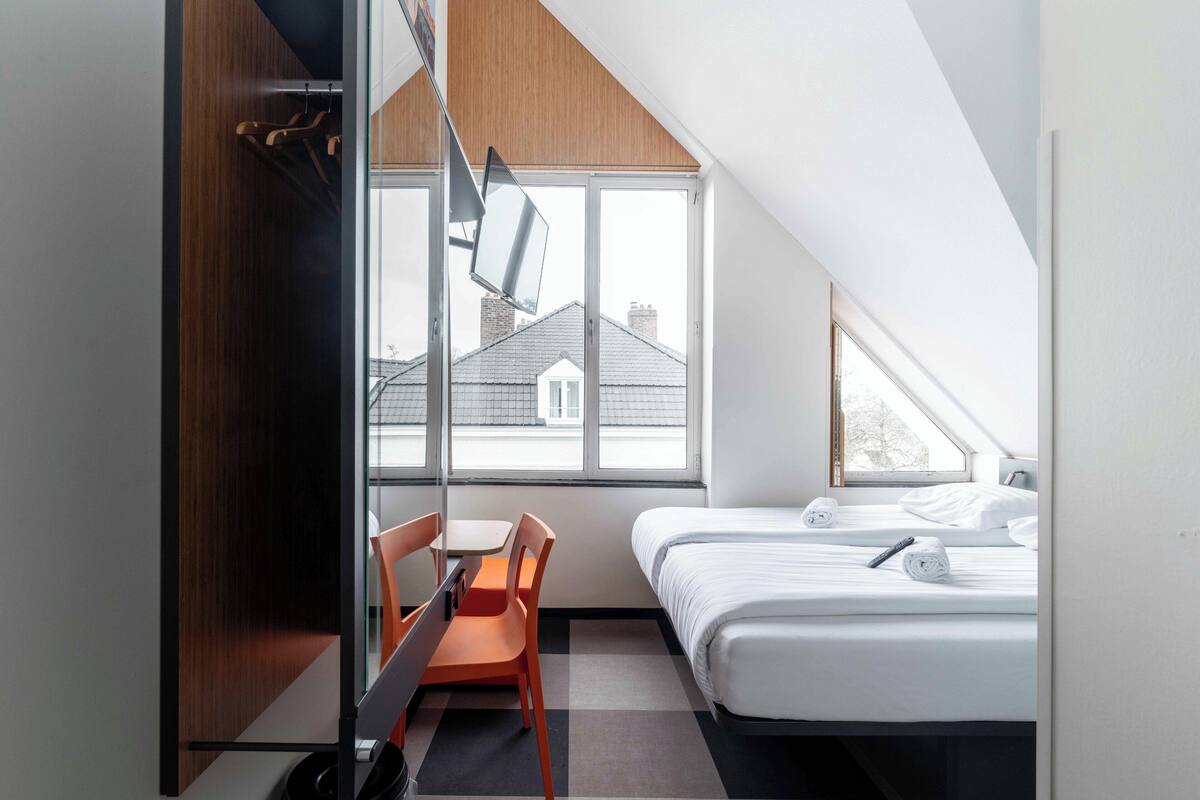 Ein modernes Hotelzimmer mit Schreibtisch, Stuhl und zwei Betten.