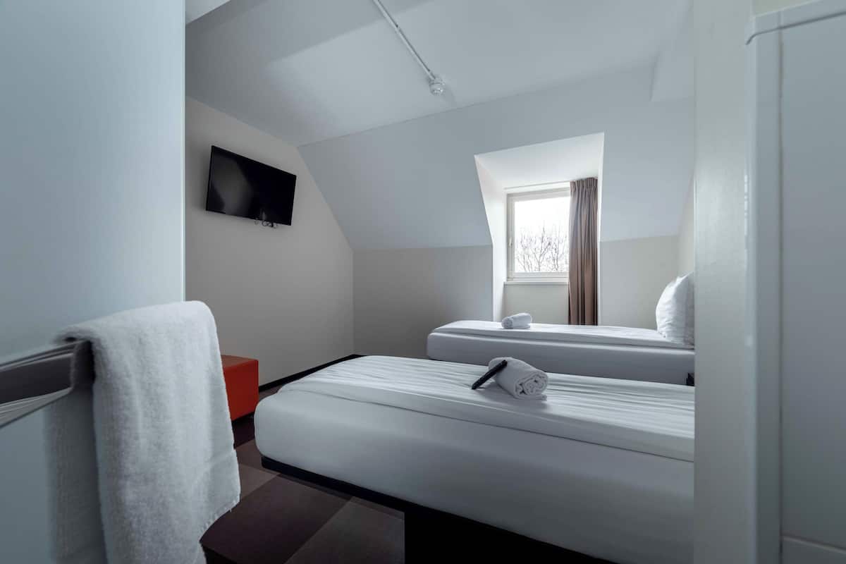 Ein modernes Hotelzimmer mit Bett, Fernseher, Fenster und einer roten Akzentwand.