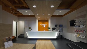 Un’area reception di un hotel dal design moderno, con una scrivania della reception, un soffitto in legno e un televisore a parete.