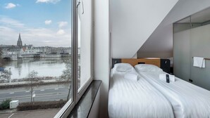 Una camera d'hotel con un letto, una finestra che offre vista su una città e un fiume, e un design moderno.