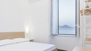 A neatly made bed with white linens in a room with a wooden headboard, a bedside table, and a window with a view of a mountain. - Lux B&B (Naples)