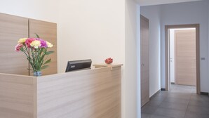 A reception desk with a vase of flowers, a digital display, and a small bowl of fruit. - Lux B&B (Naples)