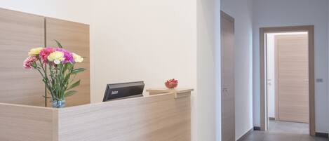A reception desk with a vase of flowers, a digital display, and a small bowl of fruit.