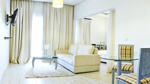 A modern living room with a sofa, a glass coffee table, a dining table with chairs, and a large window with curtains.