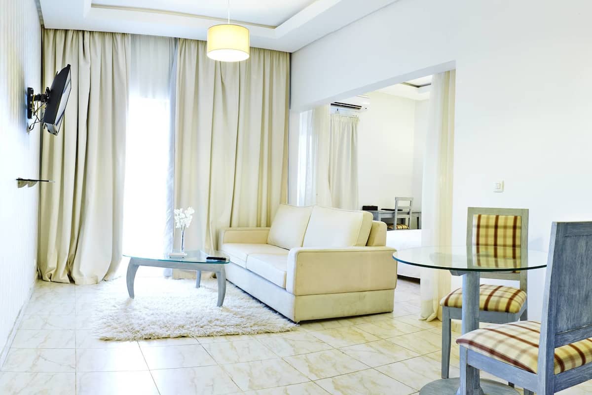 A modern living room with a sofa, a glass coffee table, a dining table with chairs, and a large window with curtains.