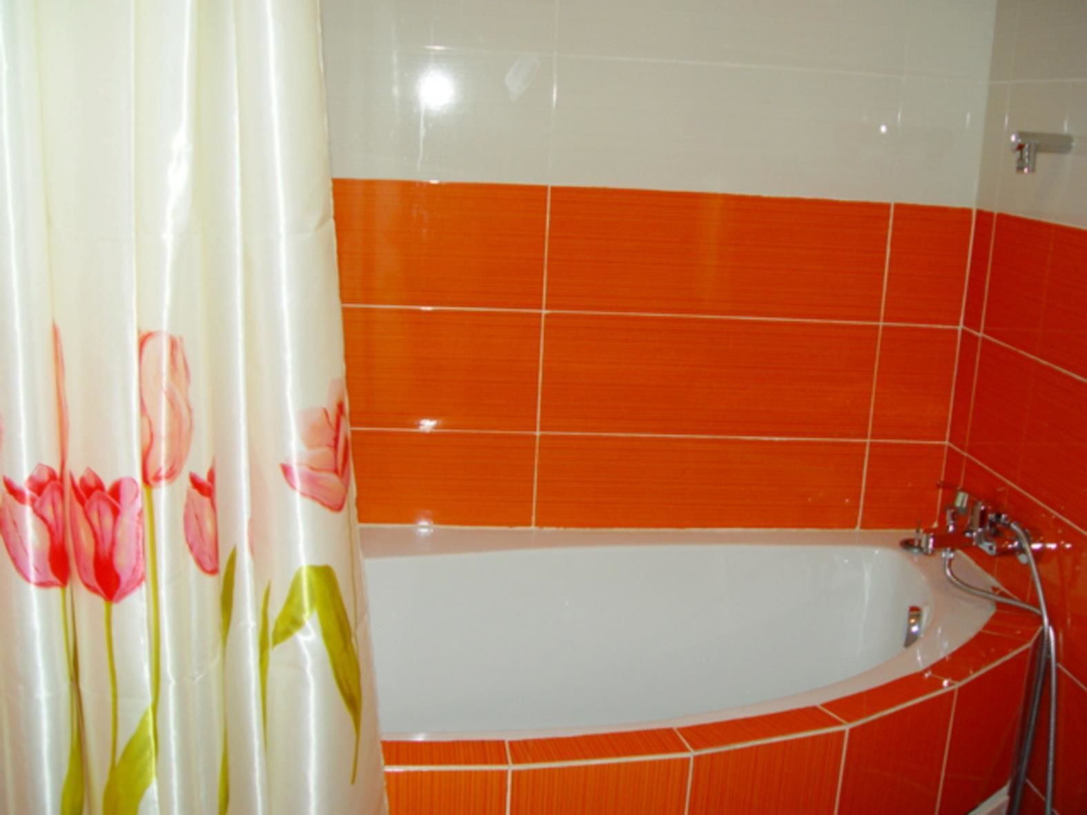 Et badeværelse med et hvidt badekar, orange fliser og en blomstret bruseforhæng.