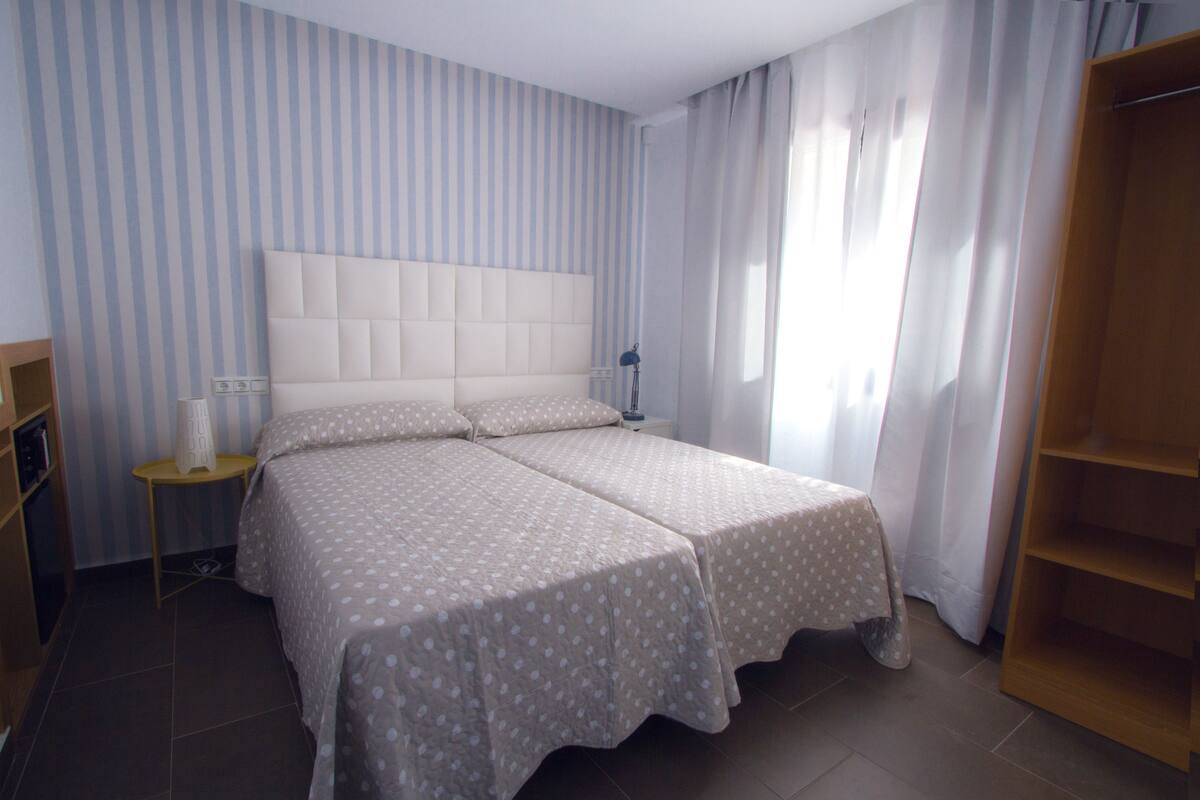 A double bed with a padded headboard, a bedside table with a lamp, and a wooden wardrobe.
