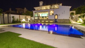 Une maison moderne à deux étages, dotée d’une piscine, d’un éclairage extérieur et d’une pelouse bien entretenue.