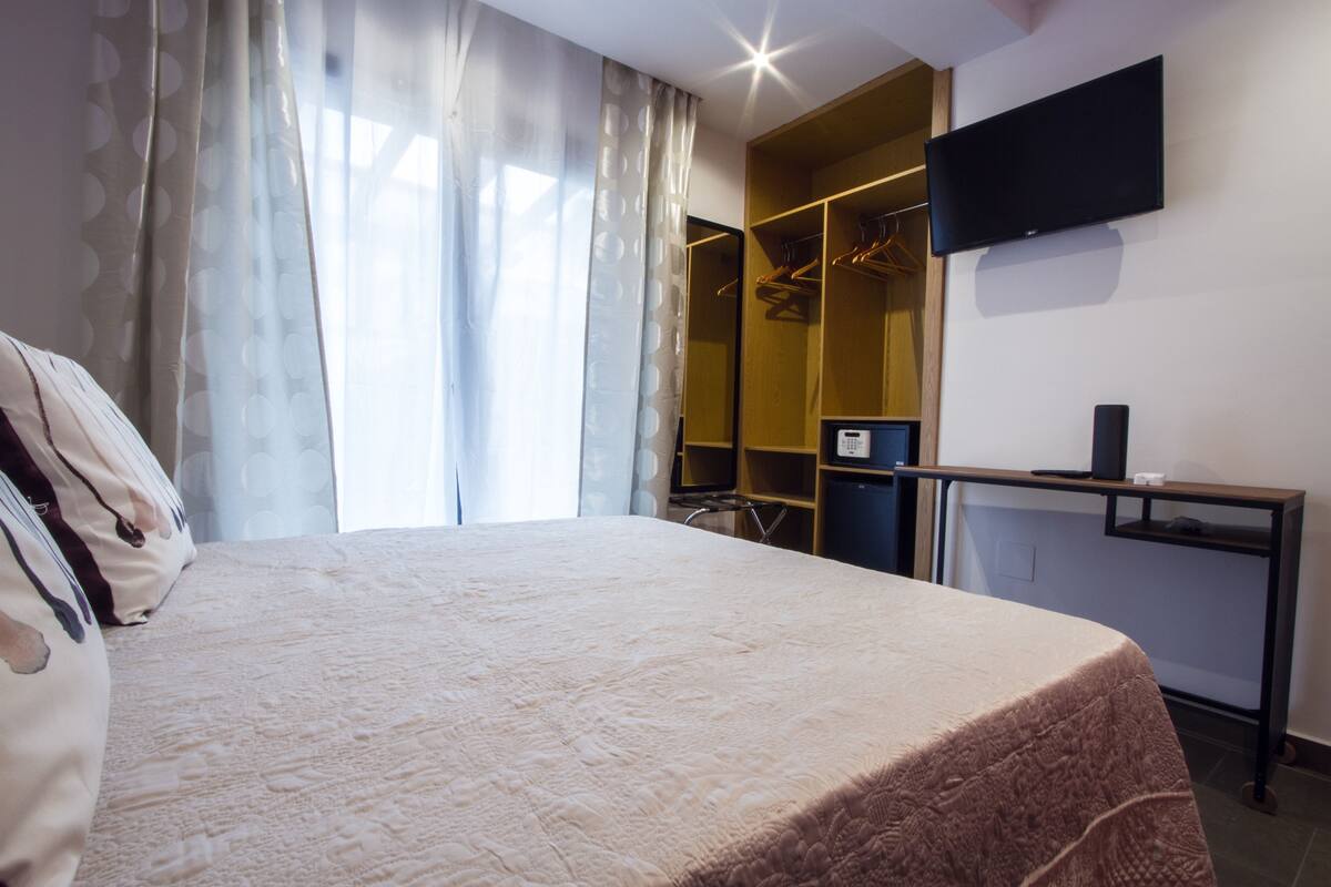 A hotel room with a bed, a desk with a computer, a TV, and a wardrobe.