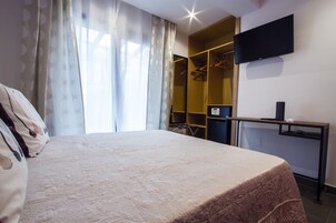 Een hotelkamer met een bed, een bureau met een computer, een televisie en een kledingkast.