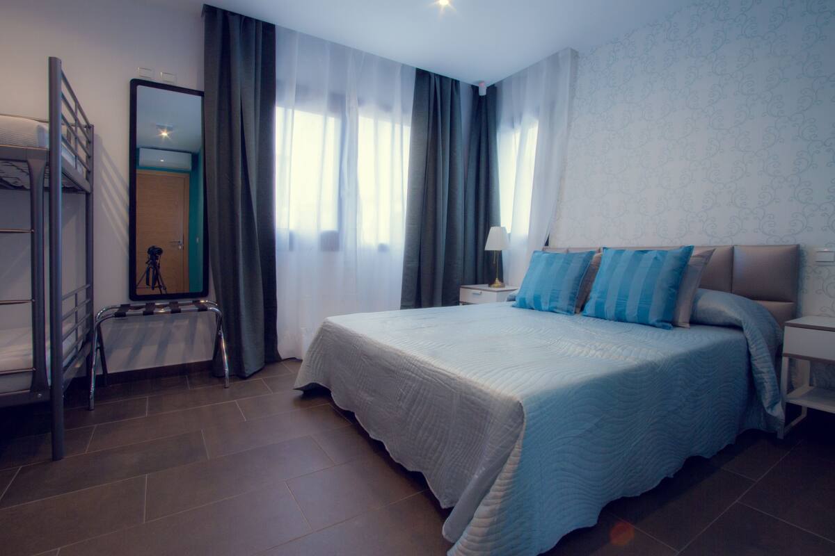 A hotel room with a bed, a desk, a chair, a mirror, and a window with curtains.