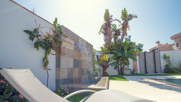 Un espace aménagé au bord de la piscine, avec des chaises longues, un mur en pierre et une petite cascade décorative.