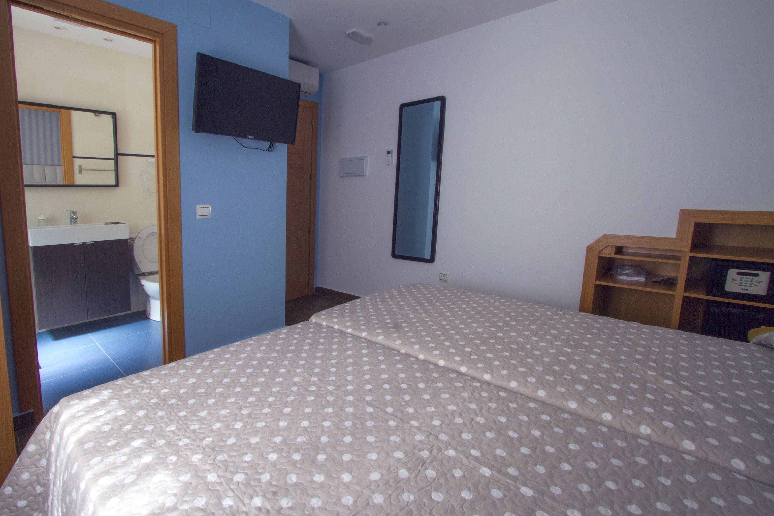 Une chambre à coucher avec un lit, une télévision, un miroir et une étagère en bois.