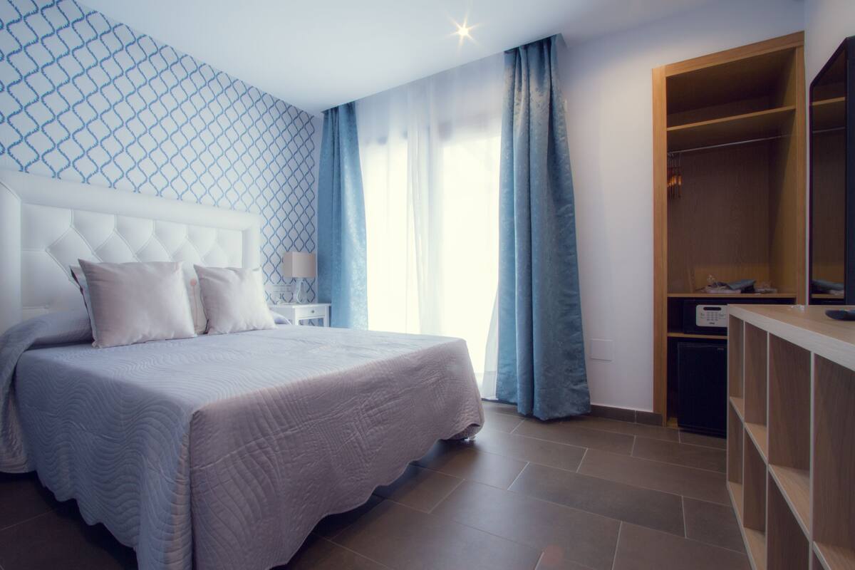 A modern bedroom with a large bed, a wooden wardrobe, and a nightstand with a lamp.