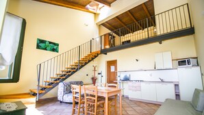 A spacious living area with a wooden staircase, a dining table, and a kitchen area.