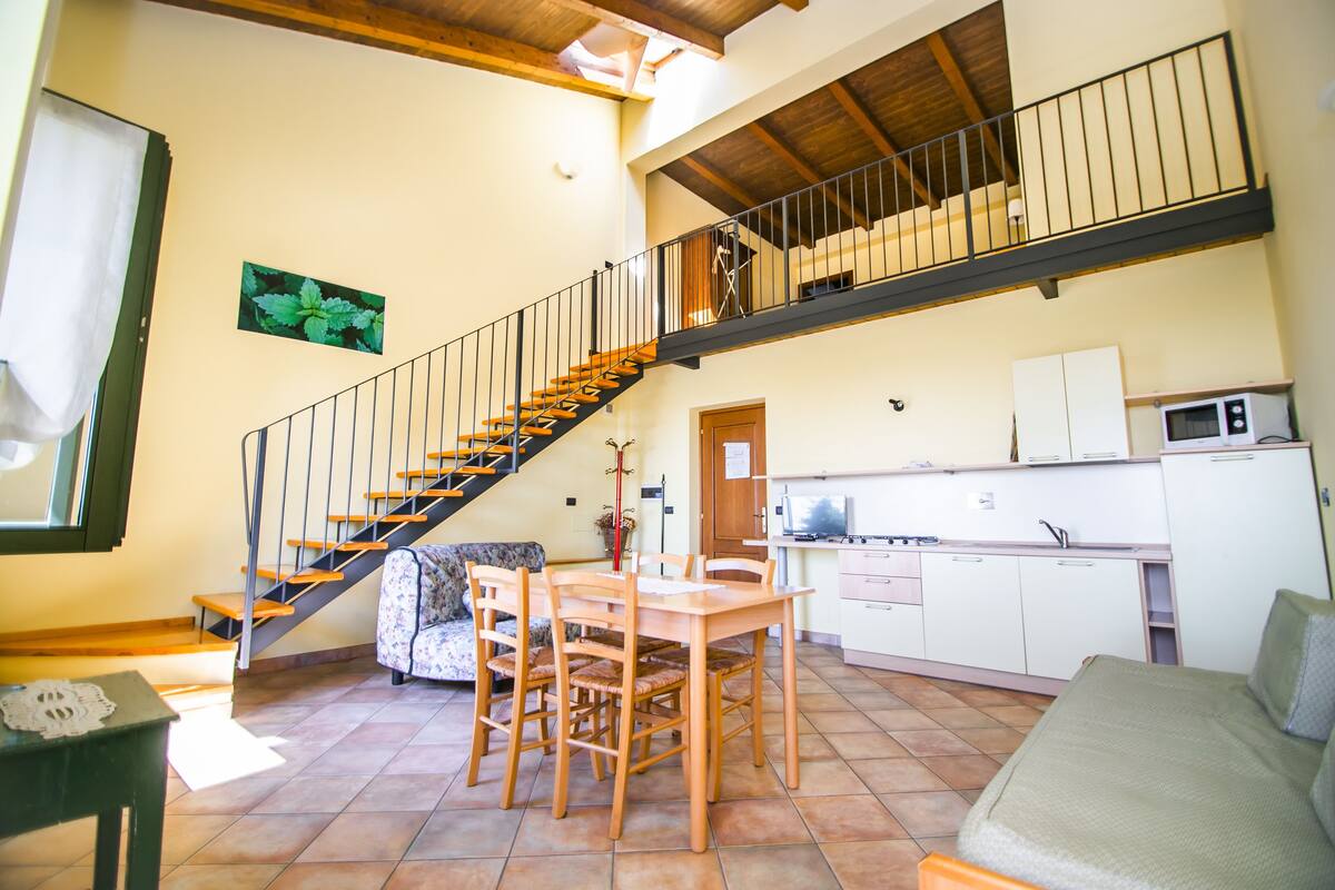 A spacious living area with a wooden staircase, a dining table, and a kitchen area.