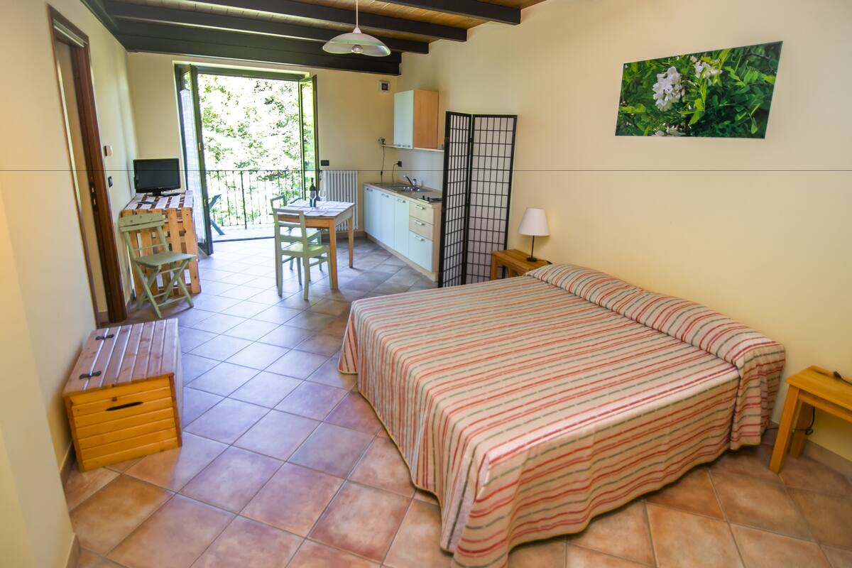 A bedroom with a bed, a desk, a chair, and a small kitchenette.