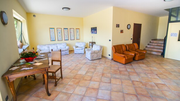 Un salón espacioso con una mesa de comedor de madera, dos sillones blancos, un sofá de cuero marrón y suelo de baldosas.
