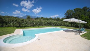 A swimming pool with a curved edge, a lounge area with chairs and an umbrella, and a mountainous backdrop.
