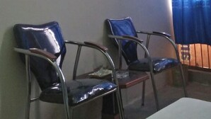 Una stanza con due sedie in metallo, una televisione appesa al muro e una finestra con tende azzurre.