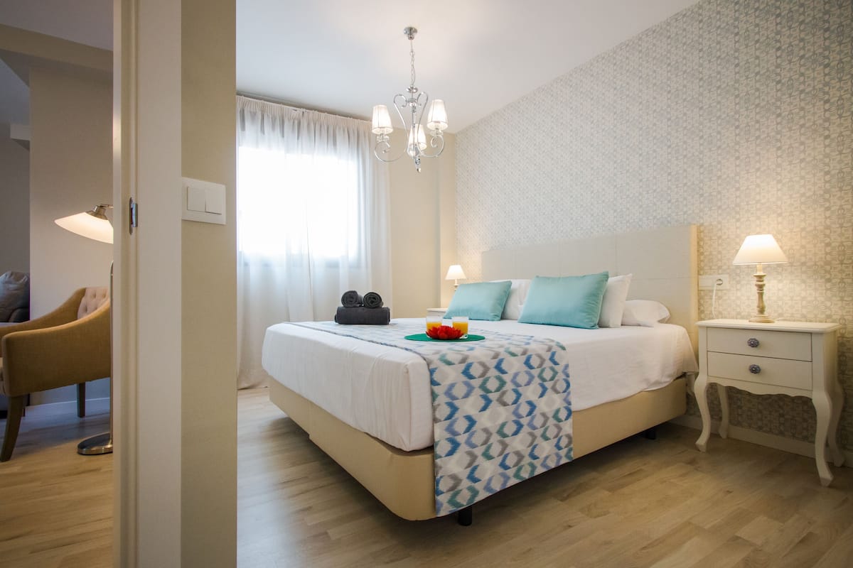 Una habitación de hotel ordenada con cama, mesita de noche y una silla.