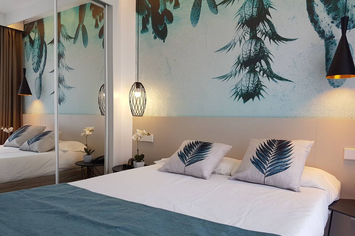 A hotel room with a large bed, a nightstand, a mirror, and a wall with a leaf pattern.